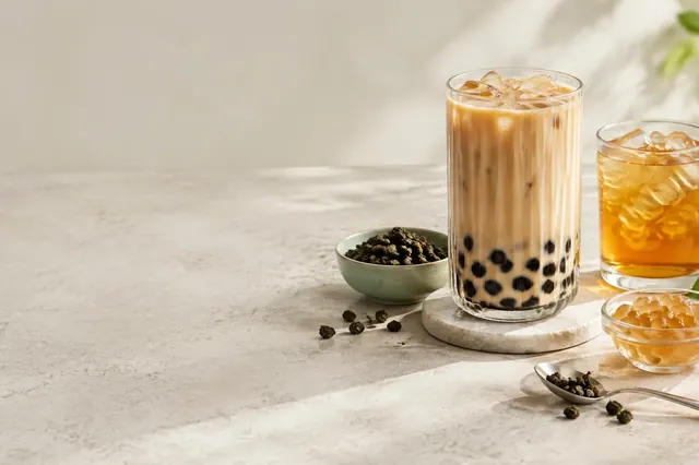 Ly trà sữa trân châu và ly trà trái cây đá bên chén trà khô và thạch